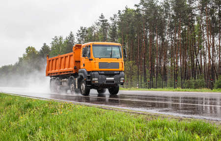 Orange dump truck with 4 axles 40 ton truck driving on a wet road against the background of a...