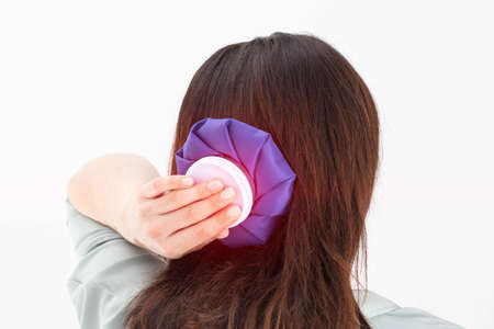 A girl holds a blue ice bag near her head to eliminate pain in the head, lowering blood pressure in case of arterial hypertension and stressの写真素材