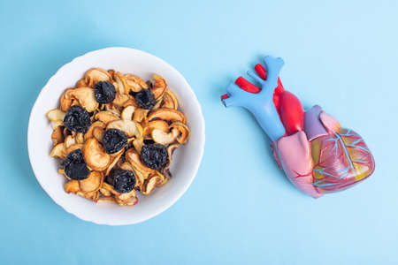 A plate with a heart mixture of dried prunes and other dried fruits on a blue background next to a...