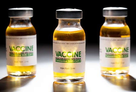 three vials with coronavirus vaccine on a black background and illuminated by a beam of light,...