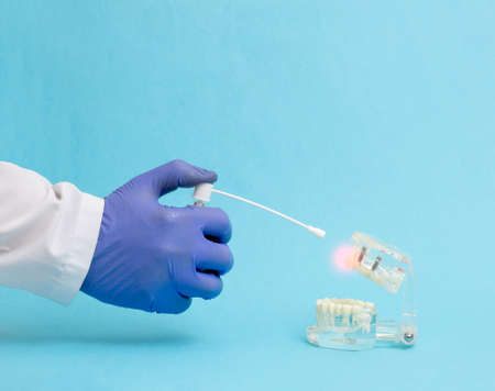 The hand of the doctor dentist on a blue background holds an anesthetic spray near the mock-up of a...