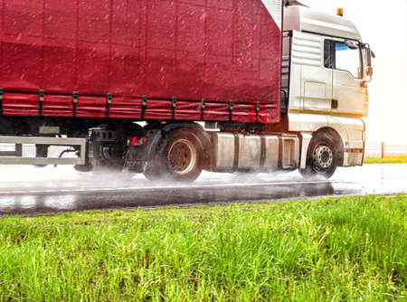 The road train transports goods in bad rainy weather. Water on the road from under the wheel. The...
