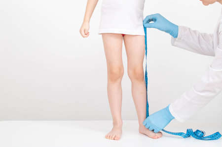 A doctor in blue gloves with a measuring tape measures the length of the legs of a 4-year-old girl. child development and growth conceptの写真素材