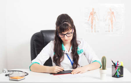 Girl doctor with a graphics tablet on the table in a medical office. Use of graphic tablets in medicine, background, interactive displayの写真素材