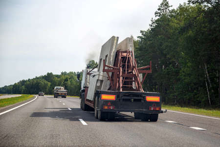 Semi-trailer truck tractor panel transporter transports reinforced concrete slabs for building a house. Transportation of spare parts for the house on the background of the forest on the highwayの写真素材