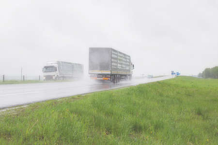 The movement of trucks of trucks with a semi-trailer and cars on a wet road in rain and fog and in poor visibility. road safety concept. Copy space for text, transportationの写真素材