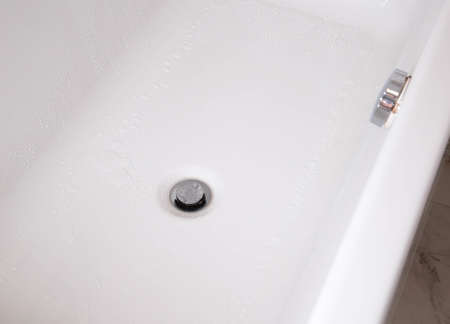 Modern silver drain plug in a new bathroom, water droplets on the walls of the bathtubの写真素材