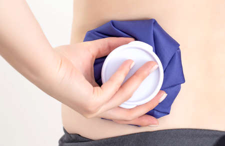 The girl is holding a medical ice bag near the injury on her back. Concept for the treatment of...