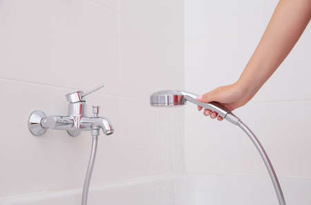The girl holds a shower on the background of the faucet in the bathroom on a white wall with tiles.の写真素材