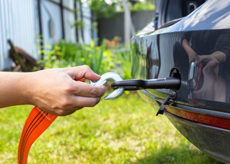 A man's hand clings a tow rope to a tow hook in a passenger car, close-up
