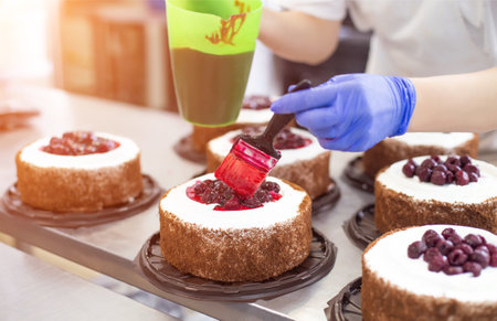 Pastry chef girl makes a cake from fresh biscuit berries and cream. Mass production of cakes and sweets, confectionery factoryの写真素材