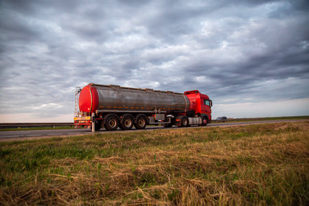 New red truck with a tanker truck transports gasoline against the background of the cloudy sky in the evening. Dangerous goods transport industry. Copy space for textの写真素材