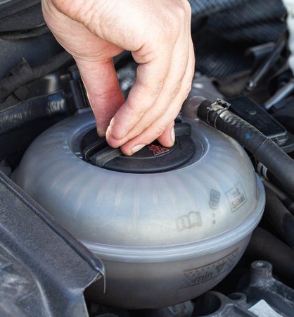A man unscrews the expansion tank cap of a car with coolant, close-up. Engine overheating problem, airlock, systemの写真素材