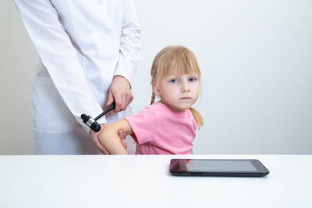 Doctor neurologist checks triceps reflex in a girl age 5 years patient. Examination by a neurologist in the office, medical, nervous system.の写真素材
