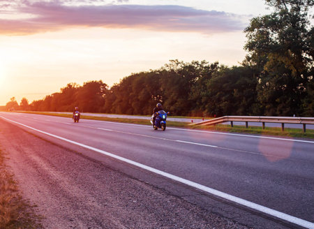 Two bikers are driving on a motorway on a country road in the summer against the background of a sunset.の写真素材