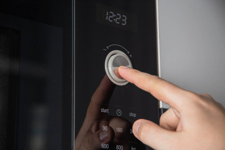A man's hand presses a button-regulator on a modern microwave oven child protection, close-up....