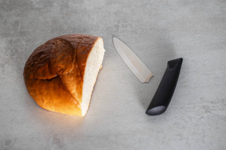 A broken ceramic knife lies on the table next to the loaf. Poor quality ceramic knife. Risk of...