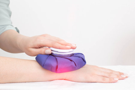 A girl applies a cooling bag of ice to the wrist joint on her arm during sprains and trauma....