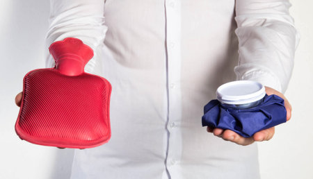 A man in a white shirt holds an ice bag and a red medical heating pad for hot water. The concept of heat and cold treatmentの写真素材