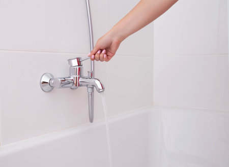 The girl's hand regulates hot and cold water in the faucets in the bathroom against a white wall.