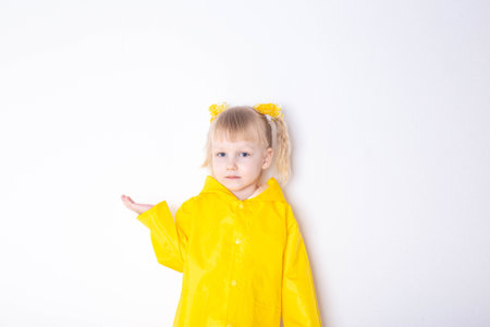 Little girl aged 3 years in a yellow raincoat on a white background. The concept of bad weather and autumn. Copy space for text, seasonalの写真素材
