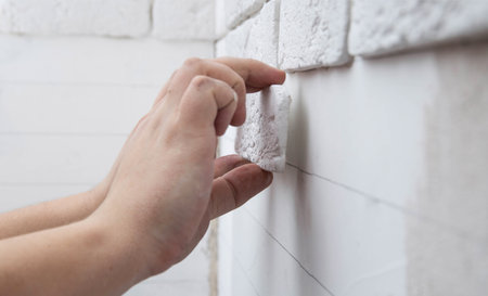 A man glues a white decorative stone in the form of a brick to the wall. Decor element, copy space for textの写真素材