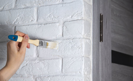 Painting decorative white stone in the form of a brick with paint. A brush in a man's hand against a wallの写真素材