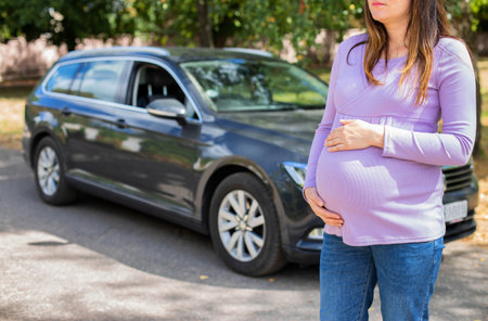 A pregnant girl with a big belly in a purple sweater on the background of a car. The concept of travel and a long trip in a car during pregnancy.の写真素材