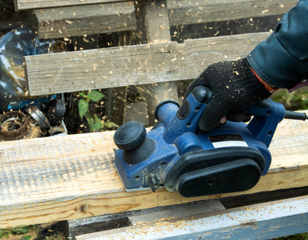 A man works with an electric tool with an electric planer, cleans old wood.