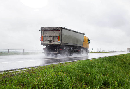 Truck with a semi-trailer grain carrier transports grain on the highway in rainy weather.の写真素材