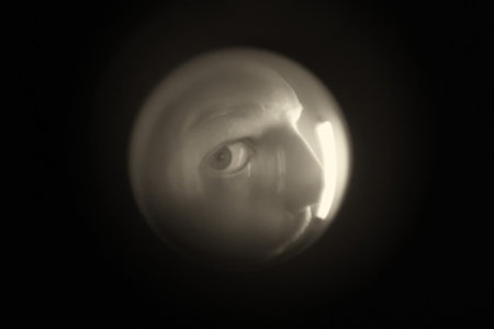 View from the peephole. A male criminal looks through the peephole to rob an apartment, hooligan. Black and white photographyの写真素材