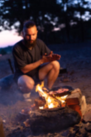 A young caucasian man with a beard prepares a dish of bacon with scrambled eggs on a fire. Cooking...