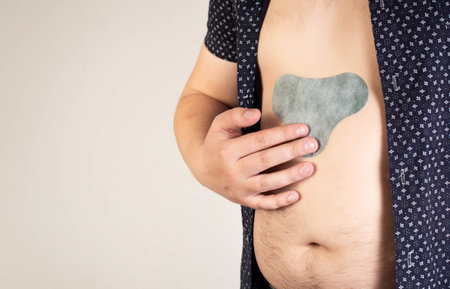 A man in a black shirt sticks an anesthetic patch on his stomach. Relieve pain and tension,...