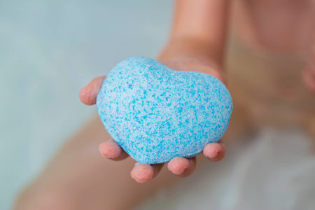 A child in the bath is holding a blue bath bomb with coconut extract.の写真素材