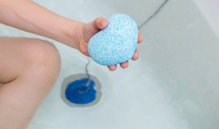 A child in the bath is holding a blue bath bomb with coconut extract.の写真素材