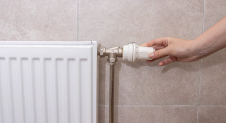 A woman regulates the gas heating in the room in order to save gas energy, taking into account the sanctions. Comfortable heating in the house.の写真素材