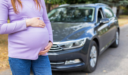 A pregnant girl with a big belly in a purple sweater on the background of a car. The concept of travel and a long trip in a car during pregnancy.の写真素材
