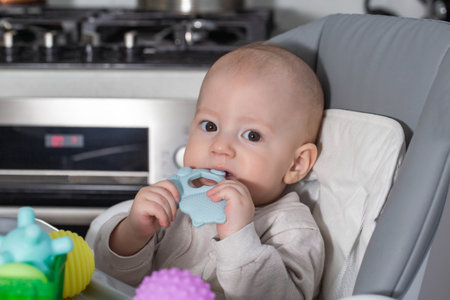 A child aged one year bites a blue medical teether. Concept massager for gums during teething in...