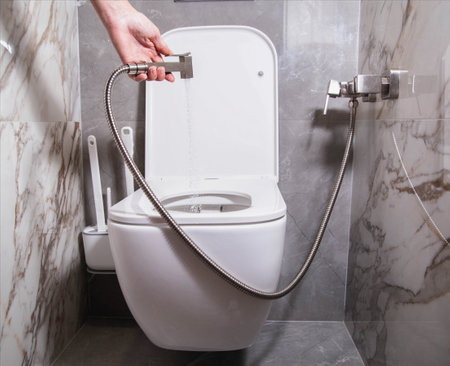The girl holds a hygienic shower in her hand against the background of a hanging toilet bowl. The concept of care for intimate places and the prevention of gynecological diseases, hygiene, comfortableの写真素材
