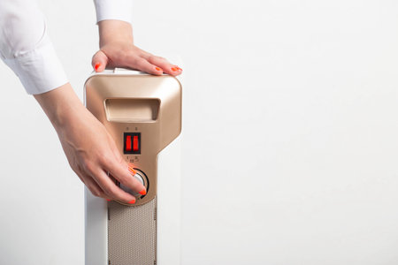 A woman s hand with a beautiful manicure regulates the room heating temperature on an electric heater. The concept of turning on the heating in the autumn-winter period. Cold in apartments. Copy space for textの写真素材