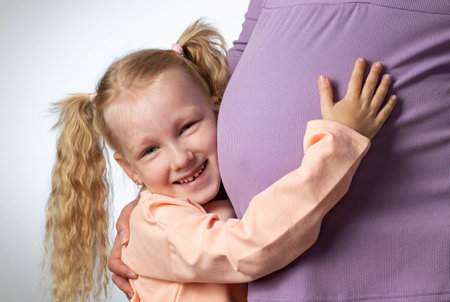 A beautiful smiling girl hugs her pregnant mother's big belly. In anticipation of a child.