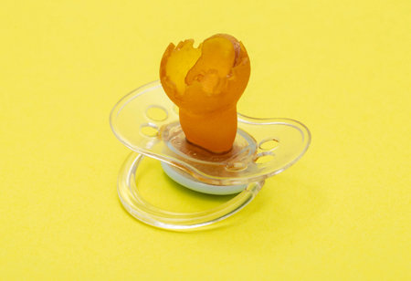 Low-quality torn baby silicone pacifier on a yellow background, close-up. Concept of the anatomical...