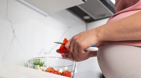 A pregnant girl prepares a vegetable salad of cucumbers and tomatoes. The concept of nutrition of pregnant women with vitamins and macronutrients in vegetables. Proper nutrition. Diet during pregnancy.の写真素材