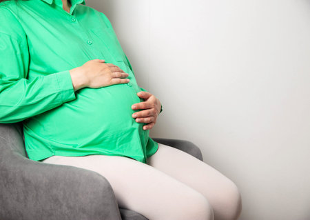 A pregnant girl in a green blouse sits on a chair and counts regular contractions before the onset of labor and a trip to the maternity hospital. Copy space for text, gestationの写真素材