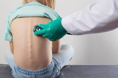 A doctor uses a stethoscope to listen to the lungs of a seven-year-old little girl. Concept of pneumonia, wheezing and bronchitis in children. Sputum discharge and cough. Treatment of viral and bacterial pneumonia. Copy space for text, inflammationの写真素材