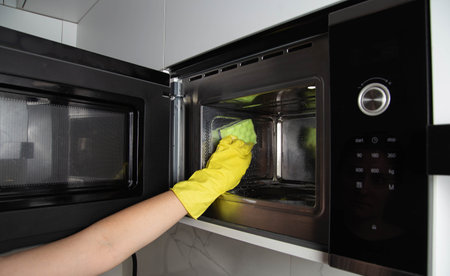A girl's hand in a yellow glove with a sponge washes the microwave oven from grease and dirt. Foam and anti-grease.の写真素材