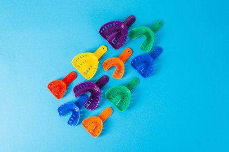 Multi-colored dental spoons for taking an impression of the dental jaw on a blue background. Orthodontics in dentistry. Dental prosthetics and crown manufacturing. Copy space for textの写真素材