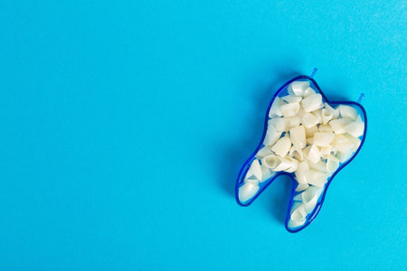 Dental crowns in the shape of a tooth on a blue background. The concept of manufacturing ceramic hypoallergenic crowns for dental prosthetics in orthodontics. Copy space for text, zirconium dioxideの写真素材