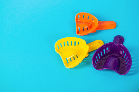 Multi-colored dental spoons for taking an impression of the dental jaw on a blue background. Orthodontics in dentistry. Dental prosthetics and crown manufacturing. Copy space for textの写真素材