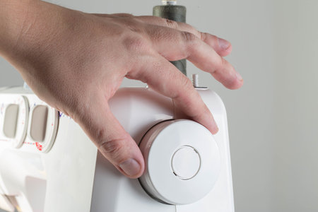 The hand of a seamstress turns the handwheel of a sewing machine while sewing, close-up.